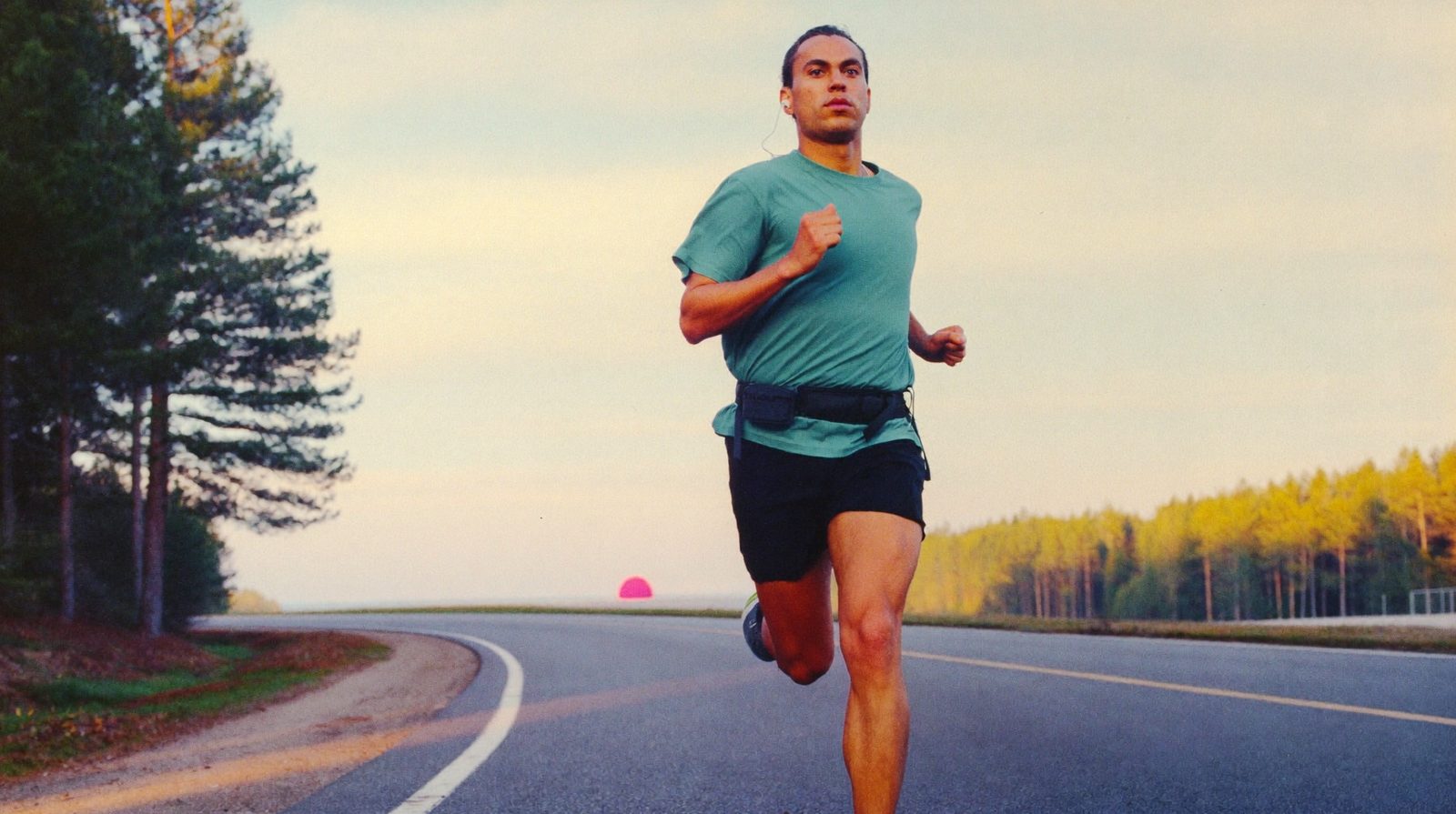 A runner in a teal shirt on an empty forest road at sunrise